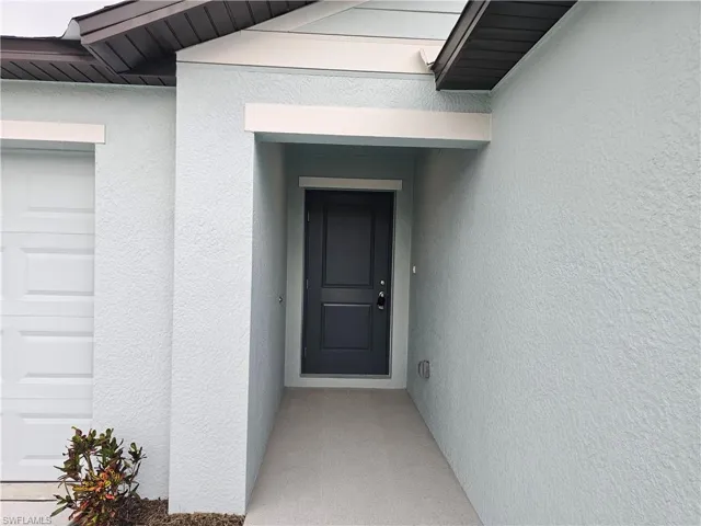 Covered entry featuring a paneled door with modern hardware, stucco exterior, and a white paneled garage door