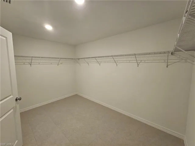 Spacious walk-in closet featuring wire shelving, recessed lighting, tile flooring, and a solid core door