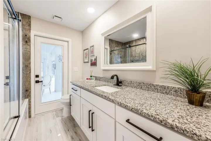 Full bathroom with shower / bath combination with glass door, vanity, plenty of natural light, and toilet