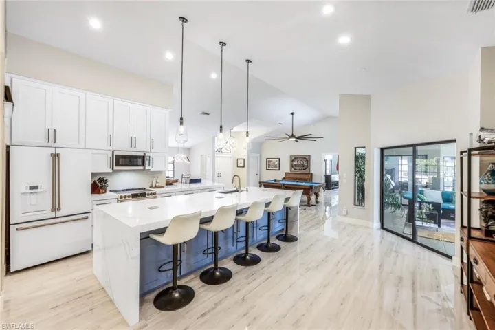 Kitchen featuring a large island with sink, white cabinets, pendant lighting, stainless steel appliances, and light hardwood / wood-style flooring