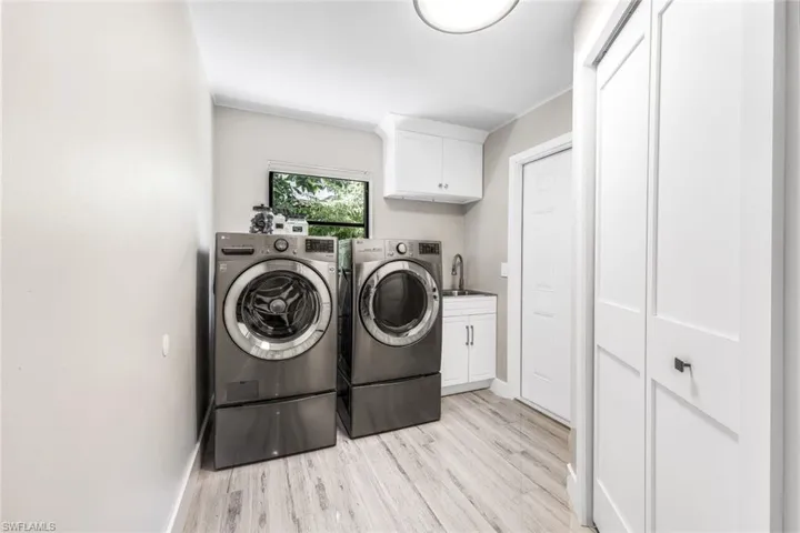 Clothes washing area with separate washer and dryer, cabinets, sink, and light hardwood / wood-style floors