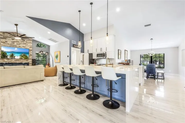 Kitchen featuring ceiling fan, pendant lighting, white cabinets, a large island with sink, and a breakfast bar area