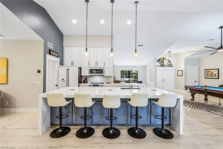 Kitchen with a kitchen breakfast bar, white refrigerator with ice dispenser, decorative light fixtures, pool table, and sink