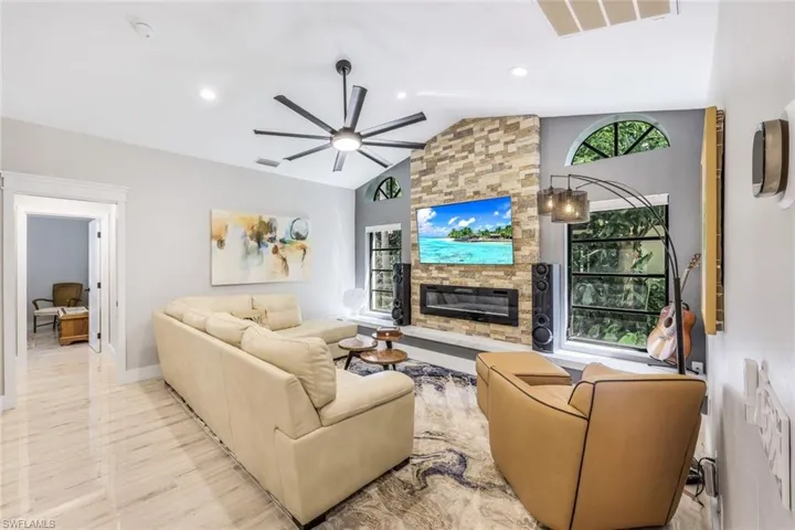 Living room with ceiling fan, a stone fireplace, and lofted ceiling