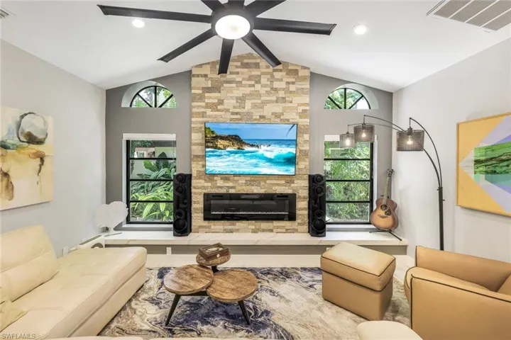 Living room featuring a stone fireplace, a healthy amount of sunlight, lofted ceiling, and ceiling fan
