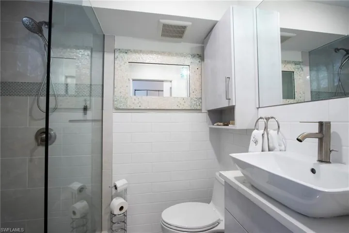 Bathroom featuring tile walls, a tile shower, toilet, and vanity with extensive cabinet space