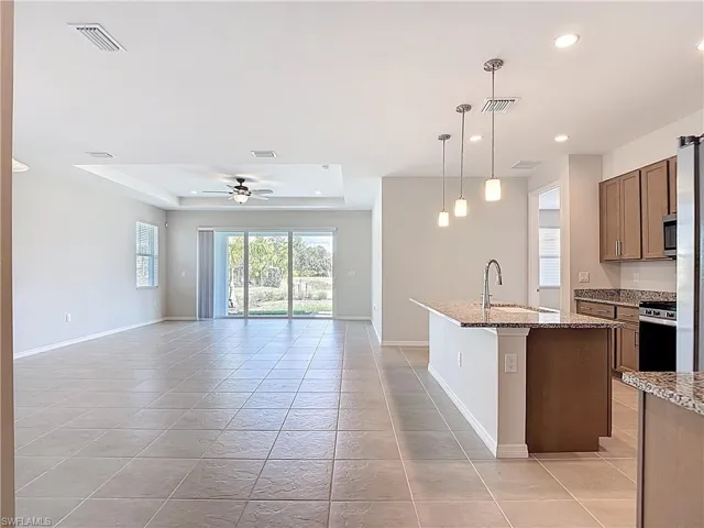 Kitchen featuring a kitchen island with sink, pendant lighting, light stone countertops, ceiling fan, and open floor plan