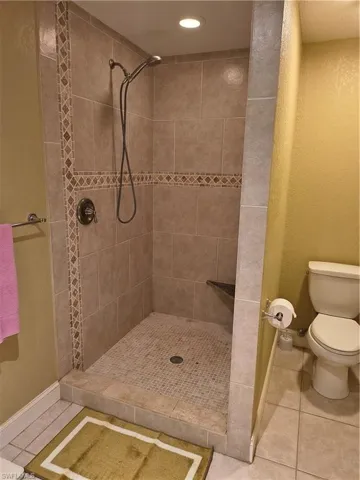 Tiled walk-in shower featuring a decorative mosaic accent band, recessed lighting, and built-in corner shelving
