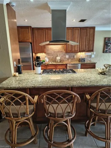 Kitchen featuring an integrated gas cooktop with stainless steel hood, stone tile backsplash, recessed lighting, and rich wood cabinetry