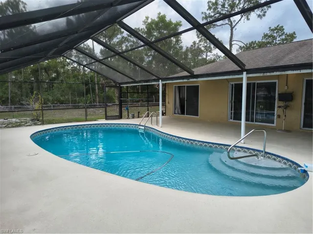 Screened-in pool area featuring a freeform swimming pool with integrated steps, a wide concrete deck, and a stucco exterior with multiple sliding glass doors