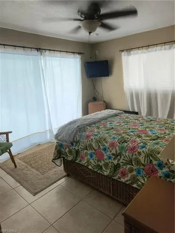 Bedroom featuring ceramic tile flooring, a ceiling fan with light fixture, and two windows with opaque curtains