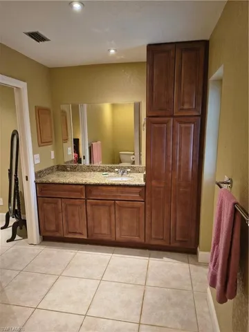 Spacious bathroom featuring a single vanity with granite countertop, integrated sink, and ample wood cabinetry