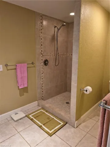 Walk-in shower featuring full-height tile surround with decorative accent band, tile flooring, and recessed lighting