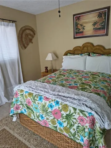 Bedroom featuring a woven headboard, light beige wall paint, a ceiling fan, and a window with white curtains