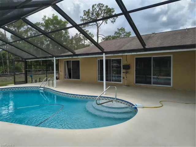 Screened-in pool area featuring a freeform swimming pool with integrated steps, a surrounding concrete patio, and direct access to the interior via multiple sliding glass doors