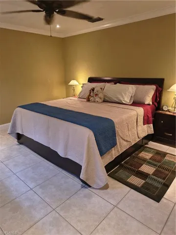 Bedroom featuring tile flooring, a dark wood headboard, crown molding, and a ceiling fan with integrated lighting