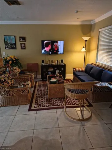 Living area featuring light-toned tile flooring, neutral wall color, crown molding, and a white window blind