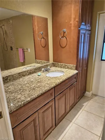 Bathroom vanity featuring a single integrated sink, granite countertop, wood-finish cabinetry, and a full-width mirror