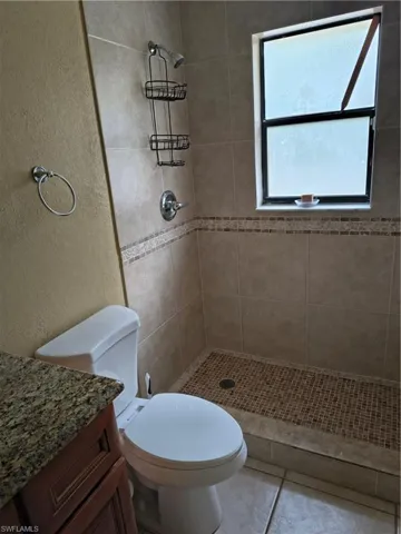 Bathroom featuring a tiled shower with mosaic floor, a white toilet, and a vanity with a granite-style countertop and wood-finish cabinetry