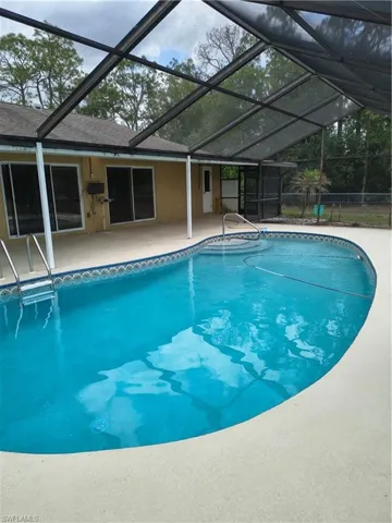 Enclosed screened pool area featuring a freeform swimming pool with steps and handrail, surrounded by concrete decking