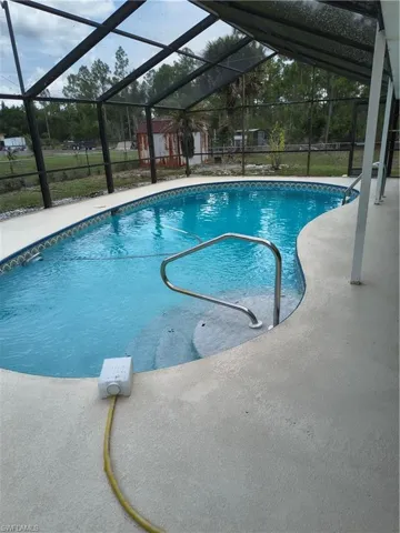 Screened-in pool area featuring a blue tiled pool with integrated steps, a stainless steel handrail, and a surrounding concrete deck