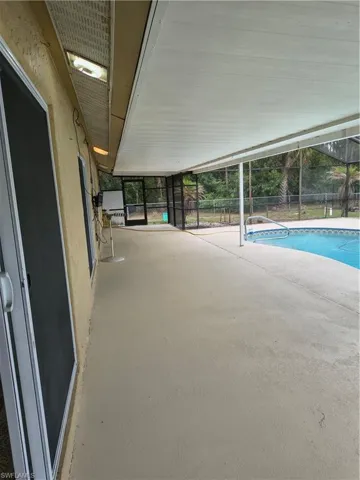 Covered patio with a light-colored concrete surface, featuring a white paneled ceiling and multiple ceiling-mounted light fixtures
