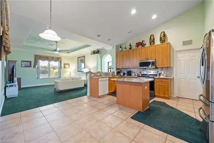 Kitchen with open floor plan, stainless steel appliances, light stone counters, decorative light fixtures, and light tile patterned floors