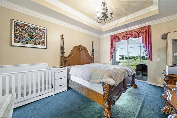 Bedroom with ornamental molding, carpet, access to exterior, a tray ceiling, and suspended lighting