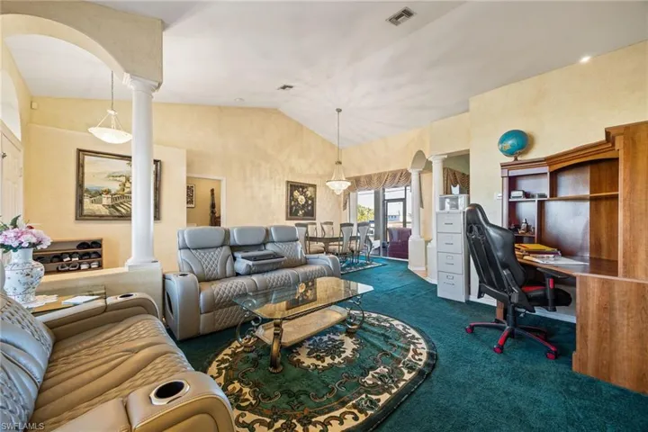 Living area featuring decorative columns, arched walkways, lofted ceiling, dark colored carpet, and an office area