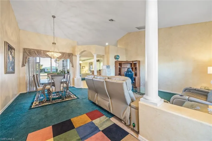 Carpeted dining space featuring ornate columns and vaulted ceiling
