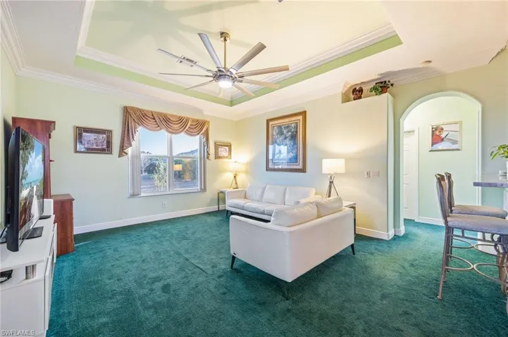 Living room featuring arched walkways, a ceiling fan, dark carpet, and crown molding
