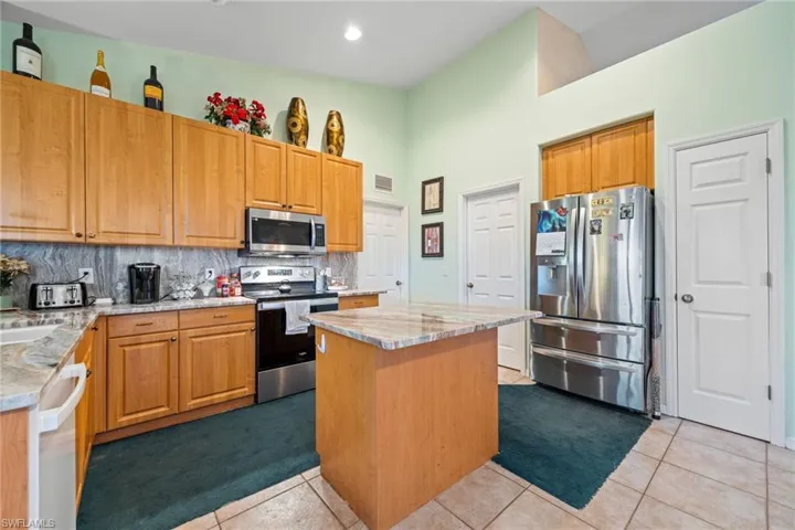 Kitchen featuring stainless steel appliances, light tile patterned floors, a kitchen island, decorative backsplash, and a high ceiling