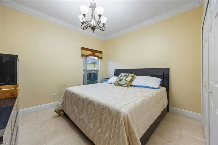 Bedroom with crown molding, suspended lighting, light tile patterned flooring, and a closet