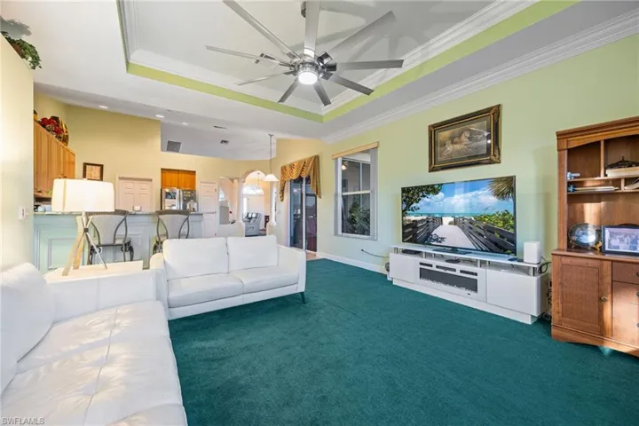 Living area with ornamental molding, a ceiling fan, arched walkways, dark carpet, and a tray ceiling