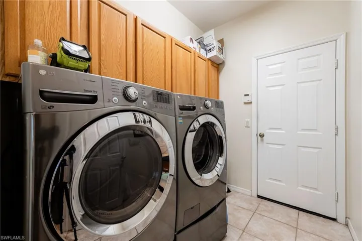 Laundry area with washing machine and dryer, light tile patterned floors, and cabinet space
