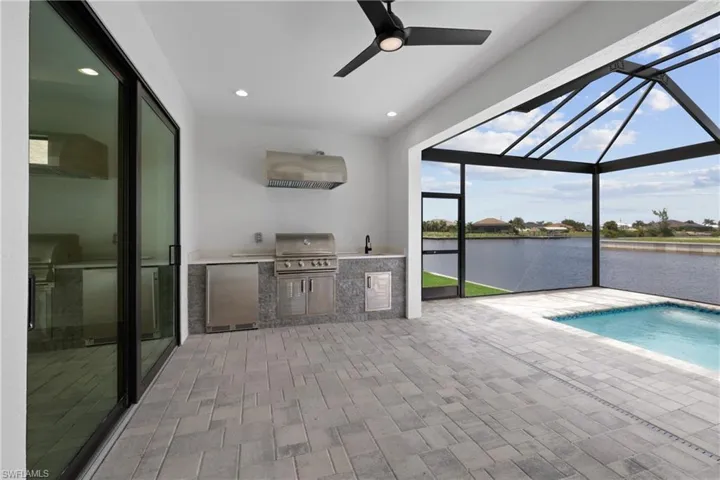 View of swimming pool with a grill, a water view, sink, and ceiling fan