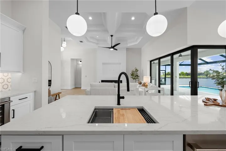 Kitchen with coffered ceiling, light stone countertops, sink, white cabinetry