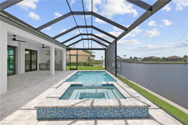 View of swimming pool with an in ground hot tub, a patio, glass enclosure, ceiling fan, and a water view