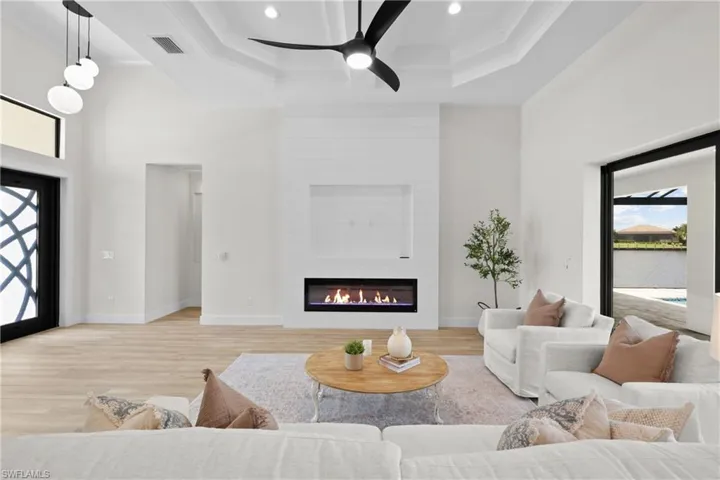 Living room with a tray ceiling, ceiling fan, a large fireplace