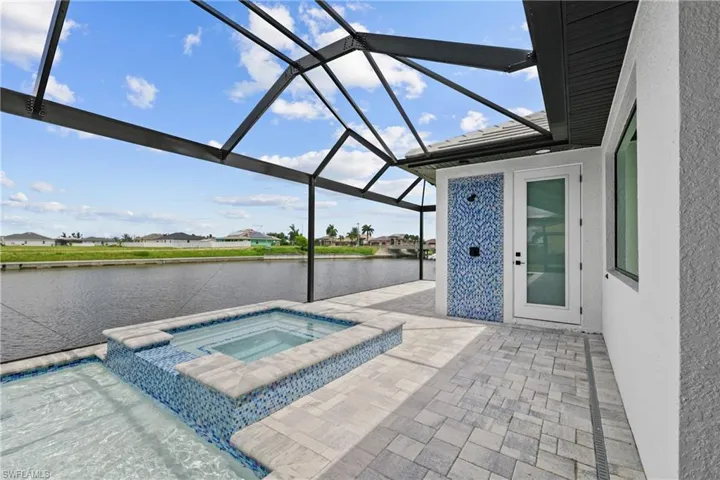 View of swimming pool with screen enclosure, an in ground hot tub, a patio area, and a water view
