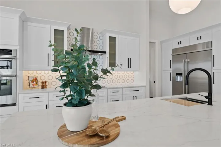 Kitchen featuring light stone countertops, appliances with stainless steel finishes, sink, decorative backsplash, and white cabinets