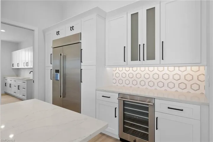 Kitchen featuring beverage cooler, built in fridge, white cabinetry,