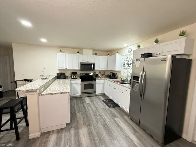 Kitchen featuring stainless steel appliances, a peninsula, a kitchen bar, white cabinetry, and light wood finished floors