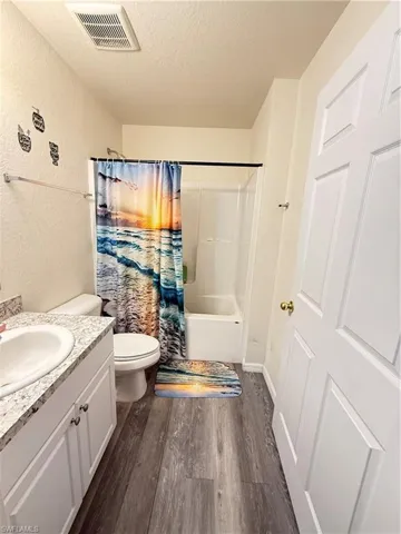 Bathroom featuring a textured ceiling, vanity, shower / tub combo, and dark wood finished floors