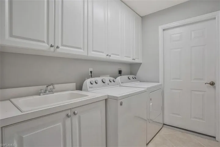 Washroom with washing machine and dryer, sink, light tile patterned flooring, and cabinets