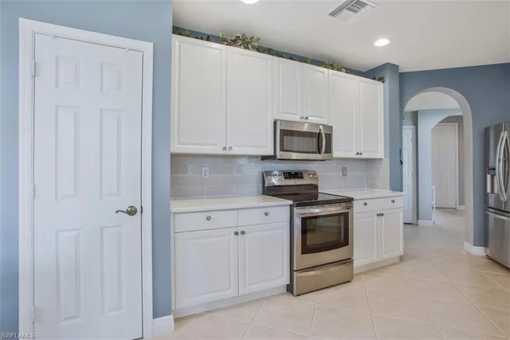 Kitchen with light tile patterned floors, backsplash, white cabinets, and stainless steel appliances