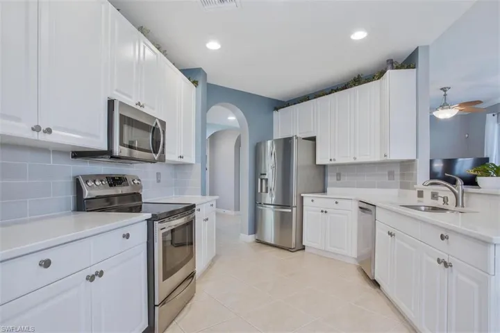 Kitchen with ceiling fan, white cabinets, light tile patterned floors, backsplash, and stainless steel appliances
