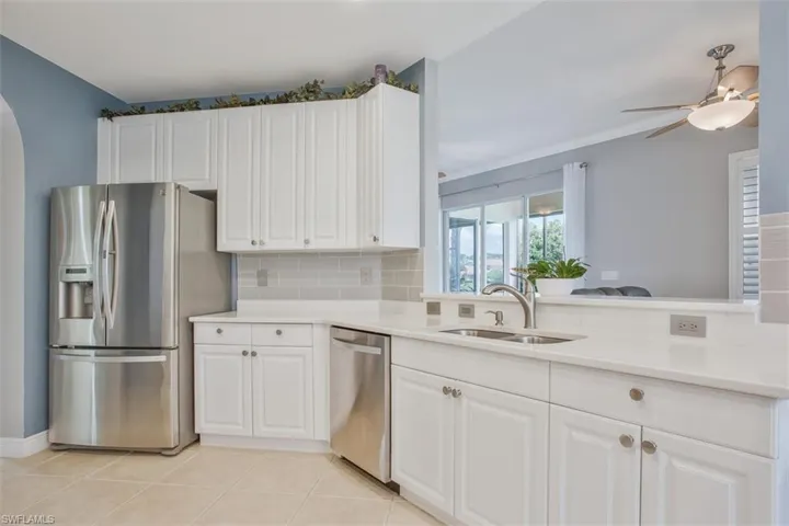 Kitchen with tasteful backsplash, appliances with stainless steel finishes, white cabinetry, ceiling fan, and sink
