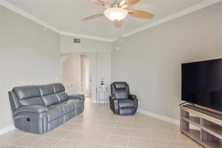 Living room with light tile patterned flooring, ornamental molding, and ceiling fan