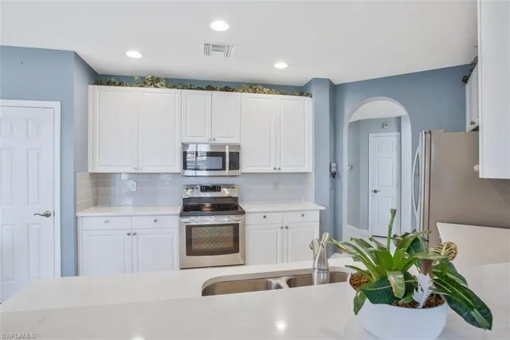 Kitchen featuring appliances with stainless steel finishes, white cabinets, light stone countertops, tasteful backsplash, and sink